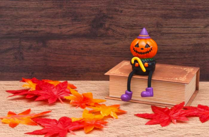 1枚目(かぼちゃのオブジェと落ち葉) ハロウィンのかぼちゃの人形と紅葉の落ち葉、秋の季節感を表す写真